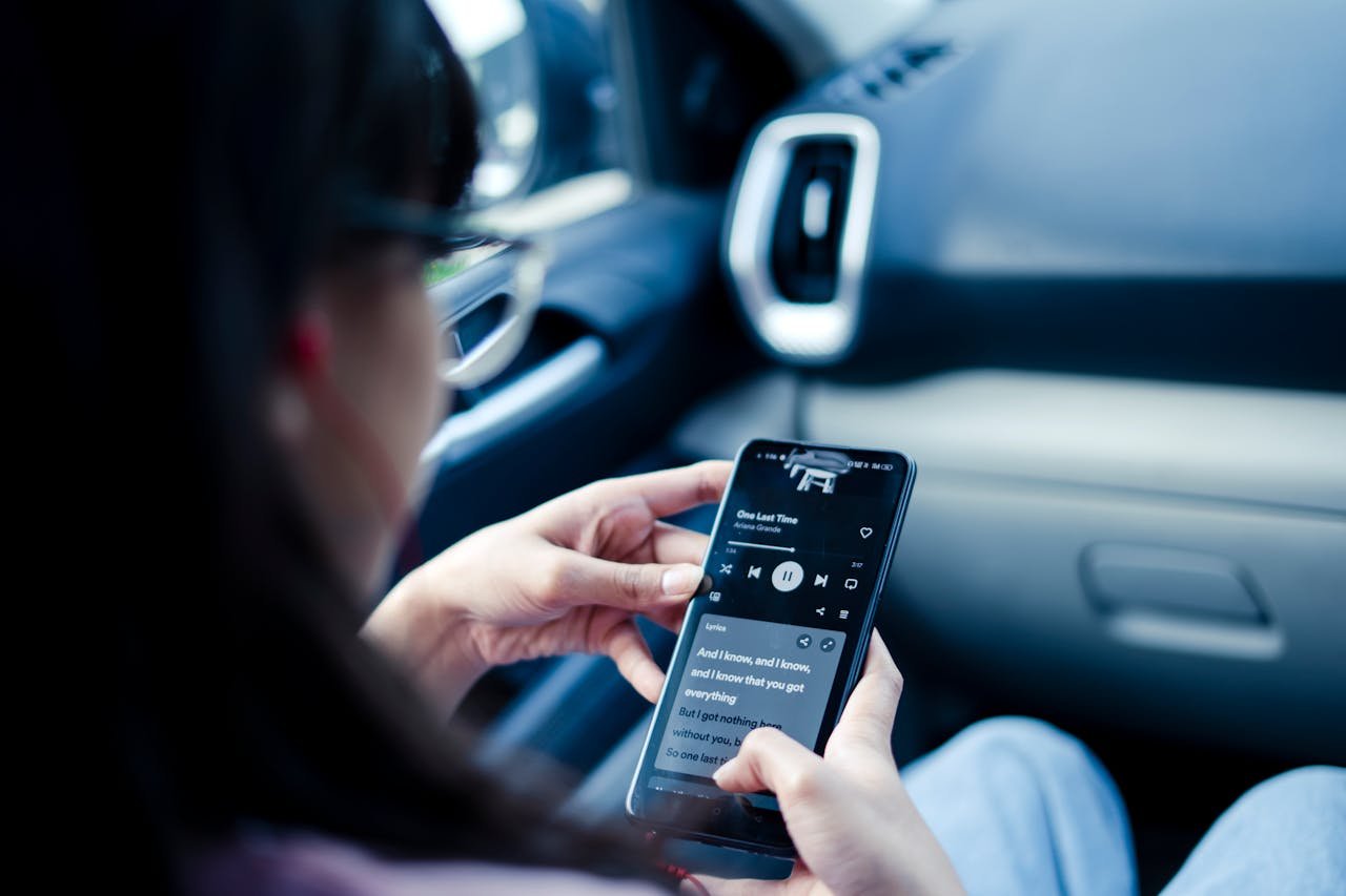 Woman using smartphone to listen to music in a car, focusing on lyrics.